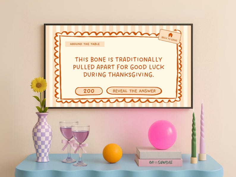 Op de afbeelding: Een ingelijst Thanksgiving-spel met de tekst "This bone is traditionally pulled apart for good luck during Thanksgiving." De sc&egrave;ne omvat een vaas met een zonnebloem, wijnglazen en een roze ballon.