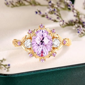 May include: A gold ring with a large oval-shaped purple gemstone surrounded by smaller white and purple gemstones. The ring has a delicate floral design.