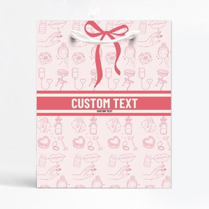 May include: Pink gift bag with a repeating pattern of beauty-related line art. The bag features a red ribbon and the words "CUSTOM TEXT" in a red banner. The pattern includes lips, hands, roses, and other beauty items.