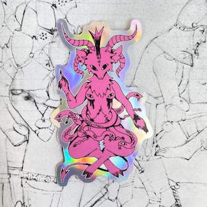 May include: A pink holographic sticker featuring a demon-like figure with horns, a crown, and multiple eyes. The figure is surrounded by snakes and has a detailed, intricate design.