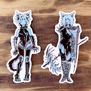 May include: Two blue and black stickers featuring illustrations of stylised female figures with cat ears and tails. The figures are wearing dark clothing and have a fierce expression.