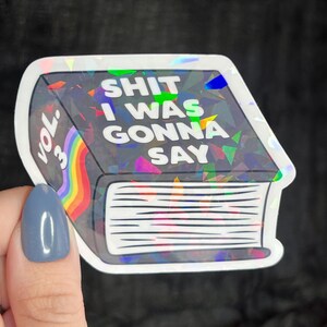 K&ouml;nnte beinhalten: Ein holografischer Aufkleber eines Buches mit dem Text "SHIT I WAS GONNA SAY" und "VOL. 3" auf dem Cover.
