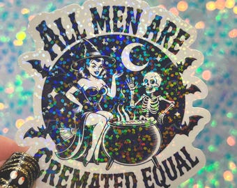 May include: A holographic sticker with the text "ALL MEN ARE CREMATED EQUAL". The sticker features a witch, a skeleton, a cauldron, bats, and a crescent moon. The witch is wearing a hat and dress.