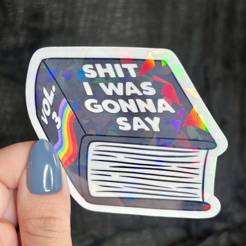 K&ouml;nnte beinhalten: Ein holografischer Aufkleber eines Buches mit dem Text "Shit I Was Gonna Say" und "Vol. 3" auf dem Cover. Das Buch ist regenbogenfarben und hat einen schwarzen Hintergrund.