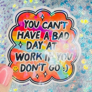 Puede incluir: Una pegatina colorida con el texto "YOU CAN'T HAVE A BAD DAY AT WORK IF YOU DON'T GO :) ". La pegatina tiene un borde blanco y un fondo de arco&iacute;ris. Incluye una carita sonriente y estrellas.