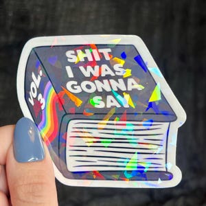 K&ouml;nnte beinhalten: Ein holografischer Aufkleber eines Buches mit einem Regenbogenr&uuml;cken und dem Text "Shit I Was Gonna Say Vol. 3" auf dem Cover.