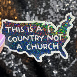 May include: A white sticker with a glittery, iridescent finish in the shape of the United States. The sticker has the text "This is a country not a church" printed in white.