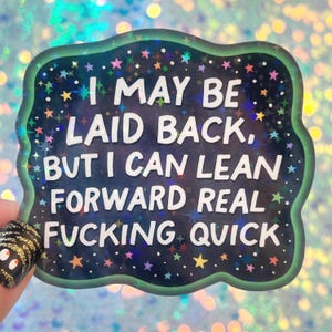 May include: A sticker with a dark blue background and a green border, decorated with colorful stars. The text reads, "I MAY BE LAID BACK, BUT I CAN LEAN FORWARD REAL FUCKING QUICK."