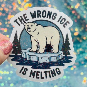 May include: A sticker with a polar bear standing on a melting iceberg. The text "THE WRONG ICE IS MELTING" is in a circular design around the bear. The sticker has a holographic, glittery finish.