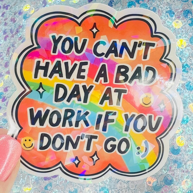 Puede incluir: Una pegatina hologr&aacute;fica con forma de nube y borde negro. El texto "YOU CAN'T HAVE A BAD DAY AT WORK IF YOU DON'T GO" se muestra en letras coloridas y en negrita. Tambi&eacute;n se incluyen caras sonrientes y estrellas.