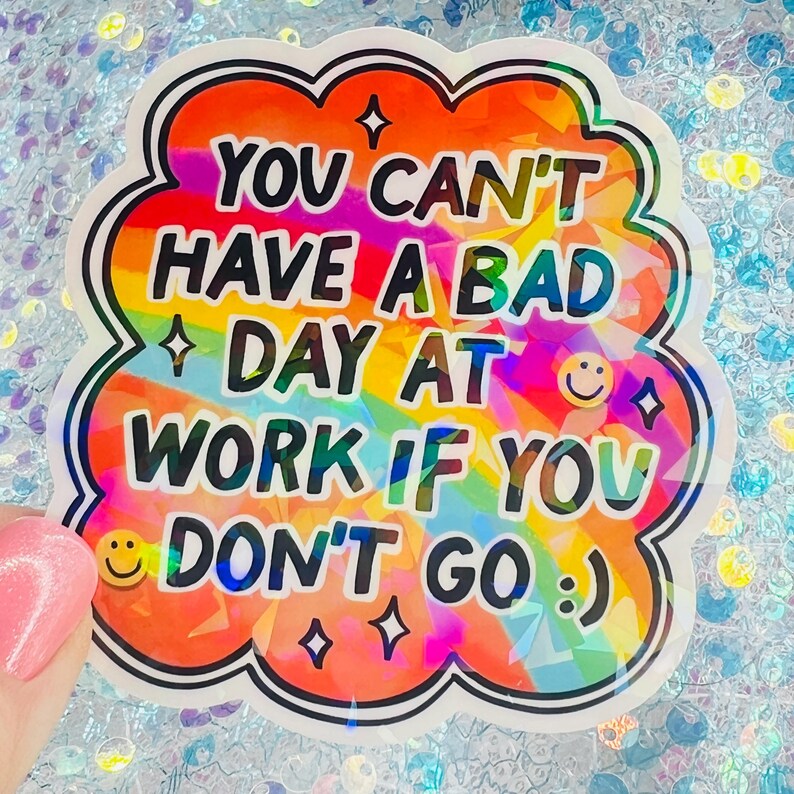 Puede incluir: Una pegatina colorida con el texto "YOU CAN'T HAVE A BAD DAY AT WORK IF YOU DON'T GO :) ". La pegatina tiene un fondo de arco&iacute;ris y un contorno negro. La pegatina est&aacute; sujeta por una persona.
