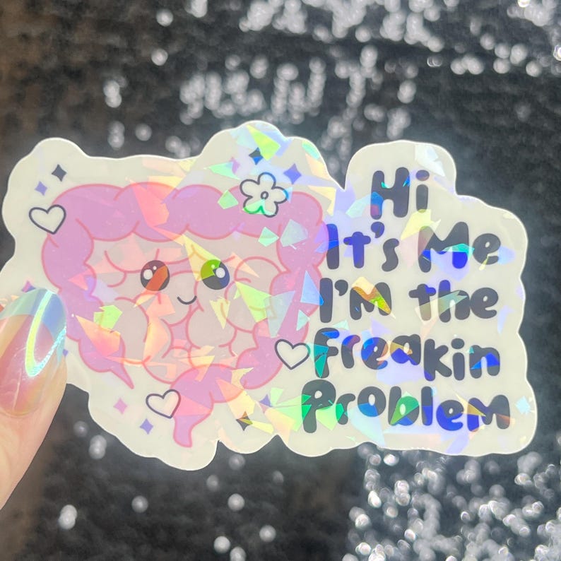 May include: A holographic sticker featuring a cartoon intestine character with a smiling face, hearts, and a flower. The sticker has the text "Hi It's Me I'm the Freakin Problem" in a playful font.