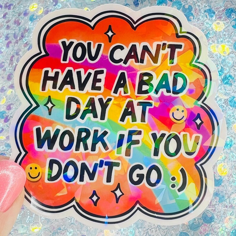 Puede incluir: Una pegatina colorida con el texto "YOU CAN'T HAVE A BAD DAY AT WORK IF YOU DON'T GO :)". La pegatina tiene un fondo de arco&iacute;ris, un contorno blanco y un borde negro. Caritas sonrientes y estrellas tambi&eacute;n est&aacute;n incluidas en el dise&ntilde;o.