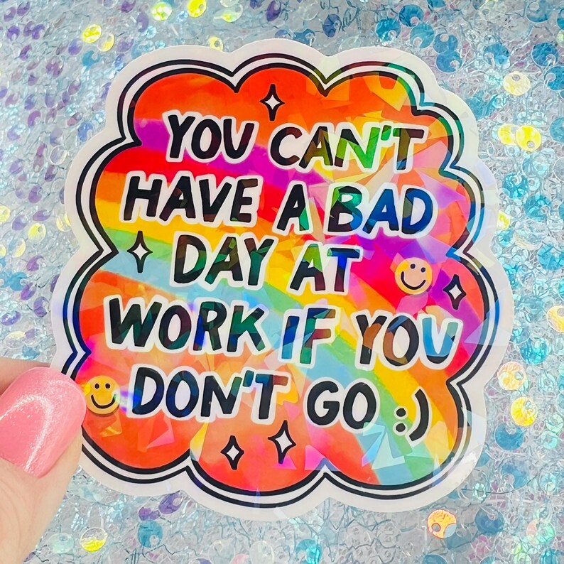 Puede incluir: Una colorida pegatina con el texto "YOU CAN'T HAVE A BAD DAY AT WORK IF YOU DON'T GO :) ". La pegatina tiene un fondo de arco&iacute;ris y un borde blanco con forma de nube. Incluye caras sonrientes y estrellas.