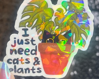 May include: A white sticker with a black cat peeking out of a pot with a green plant. The sticker says "I just need cats & plants".