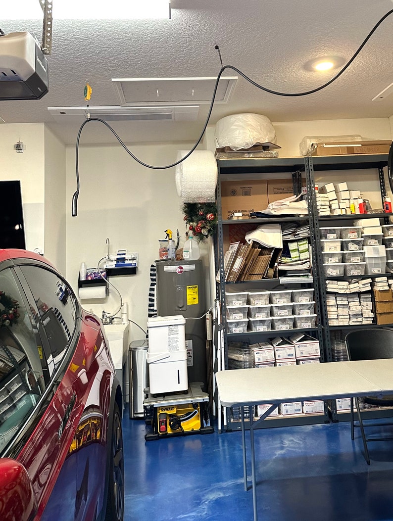The Tesla charging cable hangs high on the ceiling and over the car.
