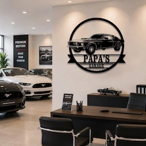May include: A circular black metal wall sign featuring a silhouette of a classic muscle car. A horizontal banner across the center displays the text "PAPA'S GARAGE" in bold, capitalized lettering. The design is mounted on a light-colored wall.