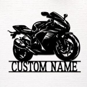 May include: Black metal motorcycle silhouette with the text "CUSTOM NAME" below. The motorcycle is a detailed depiction of a sport bike, featuring visible components like the wheels, exhaust, and fairing. The design is suitable for personalization.