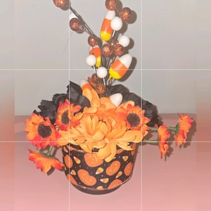 Può includere: Un centrotavola di Halloween con zucche arancioni e nere, mais dolce e fiori neri e arancioni.