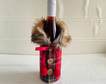 May include: A wine bottle wrapped in a red and black plaid fabric with a faux fur collar and brown buttons. The fabric has a festive Christmas theme.