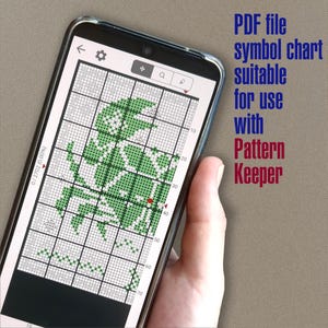 May include: A smartphone screen displaying a green and white cross-stitch pattern in the Pattern Keeper app. The screen shows a grid with numbers along the sides and a red dot marking the current position. The text "PDF file symbol chart suitable for use with Pattern Keeper" is displayed above the phone.