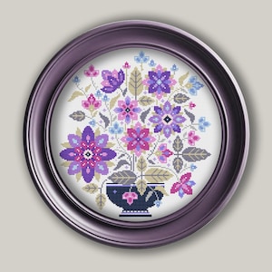May include: A framed cross-stitch embroidery featuring a bouquet of purple, pink, and blue flowers in a dark blue vase. The flowers are stylized and geometric, with a vintage aesthetic.