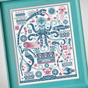 Op de afbeelding: Een ingelijst kruissteekpatroon met zeewezens in blauw, roze en wit. Het ontwerp bevat een octopus met een schedelkop, een zeemeermin, een zeeslang, een kwal en een krab, met de teksten Gloucester Sea Monster, Coelacanth, Kraken en Mermaid.