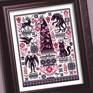 Puede incluir: Arte de punto de cruz enmarcado con varios críptidos en negro, rosa y blanco. El diseño incluye un jackalope, un cuervo, un mothman y otras criaturas, con etiquetas de texto como "Chupacabra" y "Good Cats". La obra de arte está enmarcada en un marco marrón oscuro.