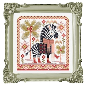 May include: Cross stitch pattern featuring a black and white zebra wearing a red and black scarf and boots, standing in front of a palm tree with red berries. The background is a white fabric with a red, pink, and gold geometric pattern.
