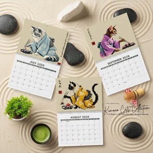 Three calendar pages for July, August, and September 2026 are arranged on a sand-raked surface, each featuring a cat in a kimono eating sushi.