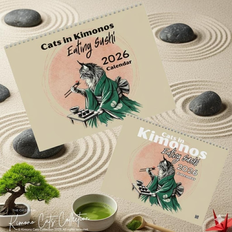 Two spiral-bound wall calendars are displayed on a sand-raked surface, both titled "Cats in Kimonos Eating Sushi 2026 Calendar" with a cat illustration.