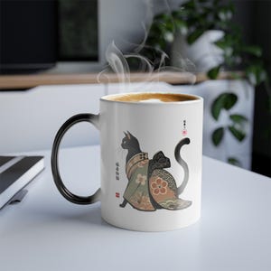 Puede incluir: Una taza de cerámica blanca con un asa negra. La taza presenta un gato negro con un kimono japonés tradicional con patrones florales y de olas. El texto "猫好き" está impreso en la taza.