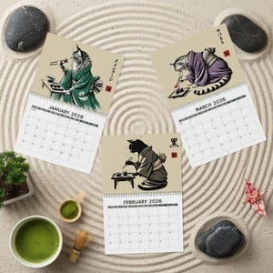 Three calendar pages for January, February, and March 2026 are arranged on a sand-raked surface, each featuring a cat in a kimono eating sushi.