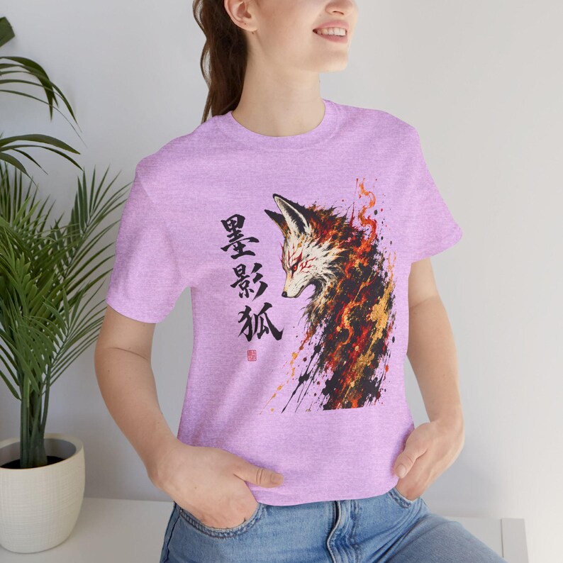 A woman wears a light purple t-shirt with a brush stroke fox design in black, orange, and gold, and Japanese characters on the left.