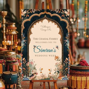 May include: A wedding welcome sign with a blue and gold floral design. The sign reads "The Chahal Family Welcomes You to Simran's Wedding Week".