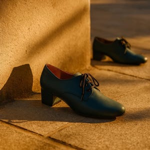 Pair of teal Oxfords on cobblestone pavement during golden hour, showing refined handmade details.