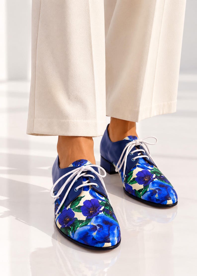Front view of blue floral leather Oxford shoes worn with ivory trousers.