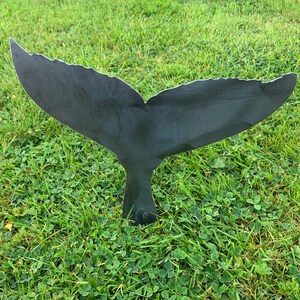May include: A black metal whale tail sculpture, standing upright in a grassy lawn.