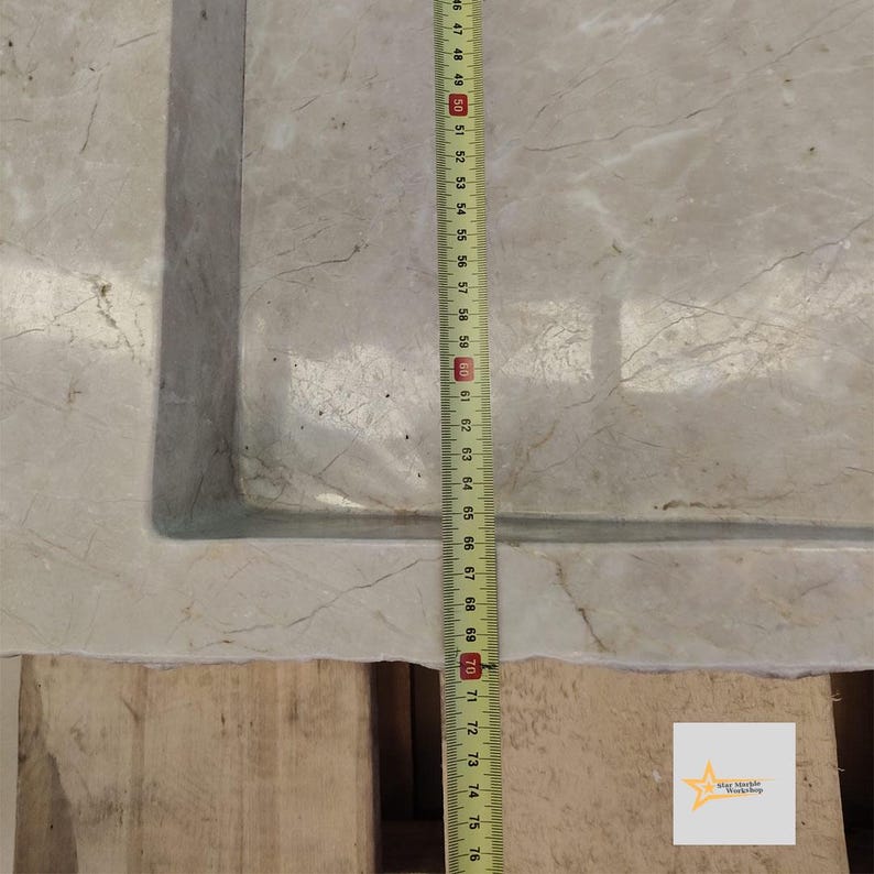 May include: A close-up of a white marble sink with a measuring tape beside it. The tape measures 76 centimeters.