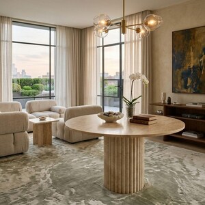 May include: A modern living room with a large round table with a fluted base. The room features neutral-toned furniture, a patterned rug, and large windows with a city view. A gold chandelier hangs from the ceiling.