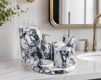 May include: A bathroom accessory set crafted from white and black marbled stone, featuring a lidded canister with a silver coral-shaped finial, a soap dispenser with a silver pump, a tumbler, a soap dish, and a toilet brush holder on a tray.