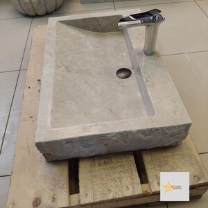 May include: A rectangular, light gray stone sink with a curved edge and a chrome faucet. The sink is sitting on a wooden pallet.