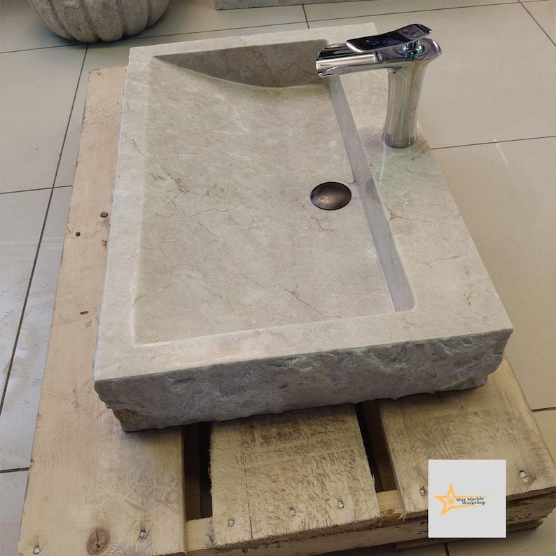 May include: A rectangular, light gray stone sink with a curved edge and a chrome faucet. The sink is sitting on a wooden pallet.