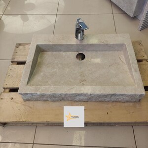 May include: A rectangular, light gray marble sink with a single faucet and a drain hole. The sink is sitting on a wooden pallet.