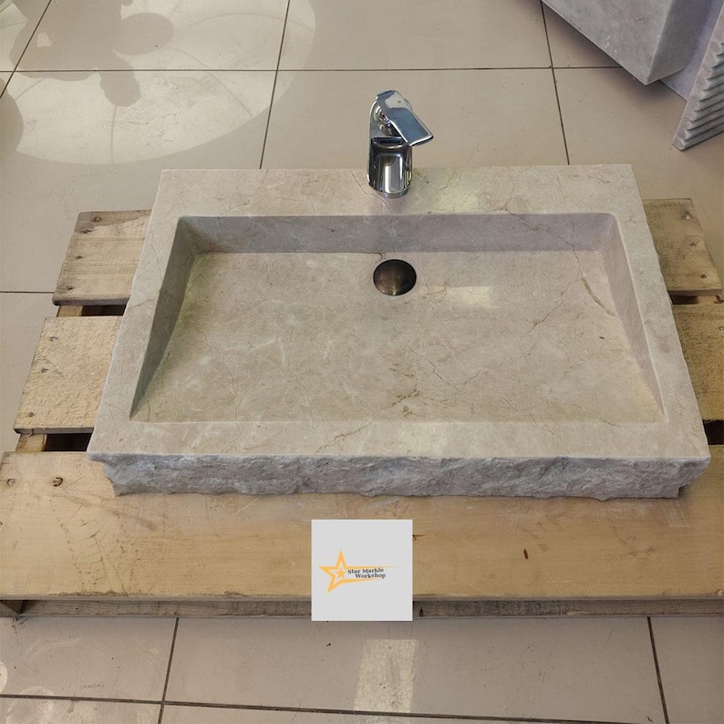 May include: A rectangular, light gray marble sink with a single faucet and a drain hole. The sink is sitting on a wooden pallet.