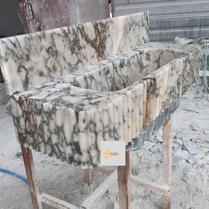 May include: A rectangular marble sink featuring a white base with prominent dark grey and brown veining. The front exterior of the basin displays a vertical fluted texture. A matching marble backsplash is attached to the rear of the sink unit.