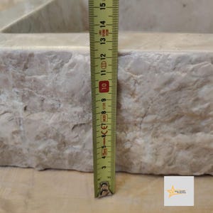 May include: Close-up of a white marble sink with a yellow measuring tape next to it. The tape measures 10 inches.