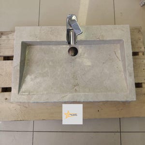 May include: A rectangular, light gray marble sink with a single hole for a faucet. The sink has a slightly rounded edge and is mounted on a wooden surface. A chrome faucet is installed in the sink.