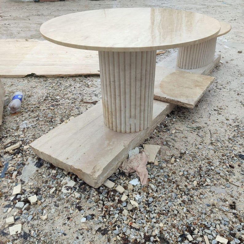 May include: A light beige stone table with a round top and a fluted column base. The table sits on a rectangular stone base. The table is approximately 36 inches in diameter.