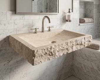 Puede incluir: Un lavabo rectangular montado en la pared, hecho de piedra natural beige con una textura exterior rugosa y cincelada, y una cubeta interior lisa. Incluye un orificio de drenaje central y un grifo de níquel cepillado con dos manijas laterales.